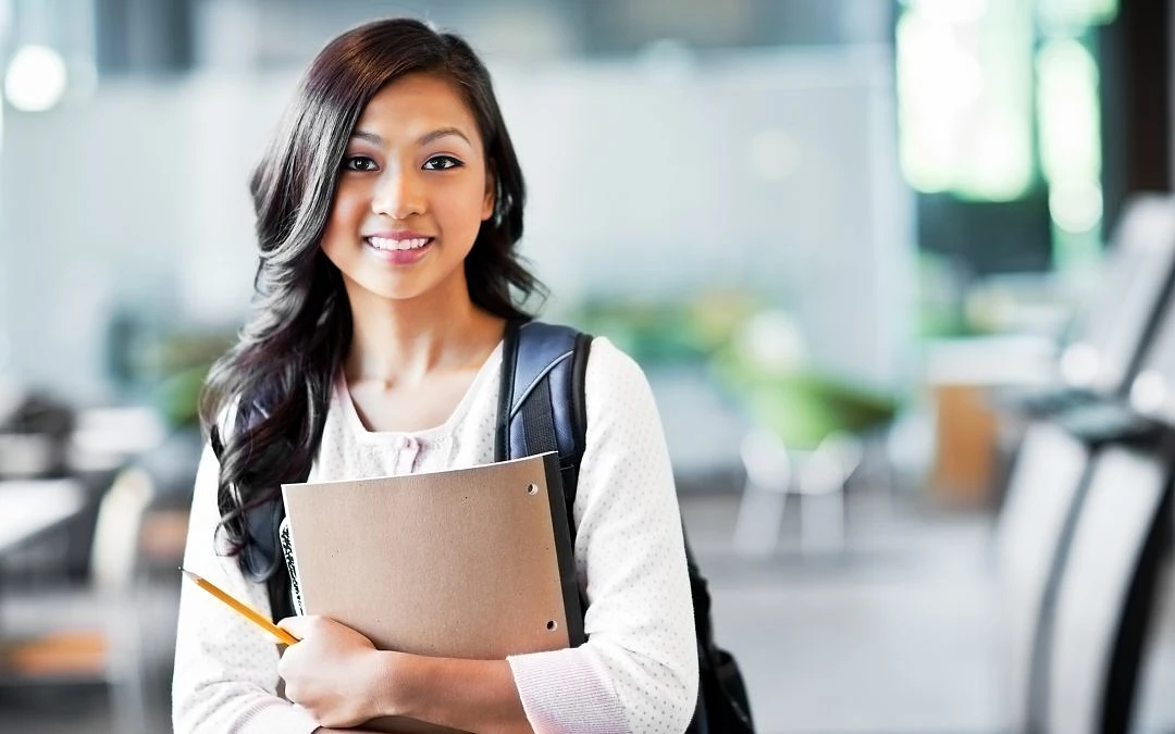 A student stands holding a notebook with a backpack on